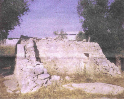 Foto di Cristiano Villani, del Menhir Santa Loja (2004). Il monolite sporge dal muro del rudere a sinistra, sul lato esposto all’ incirca a Nord della costruzione. La foto corrisponde alla vista che si aveva dalla ampia strada della zona industriale
